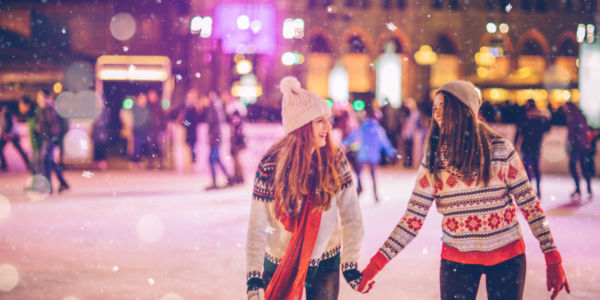 Two women ice skating at a downtown rink.